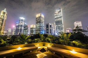 A nighttime cityscape with illuminated skyscrapers and a well-lit outdoor seating area with plants. - La Boheme Rooms and Coffee (Jakarta)