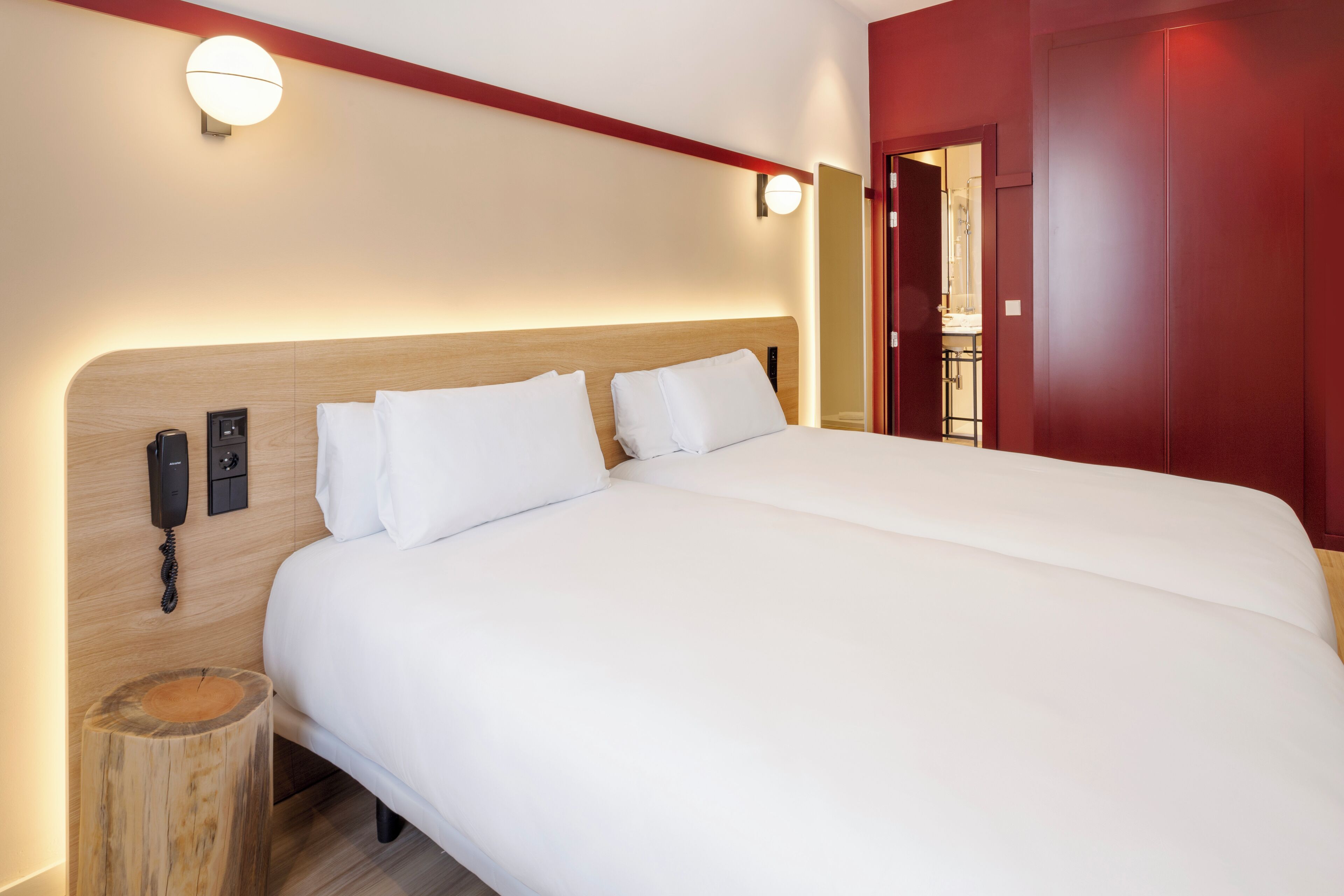 A hotel room with a large bed, a bedside telephone, and a wooden nightstand.