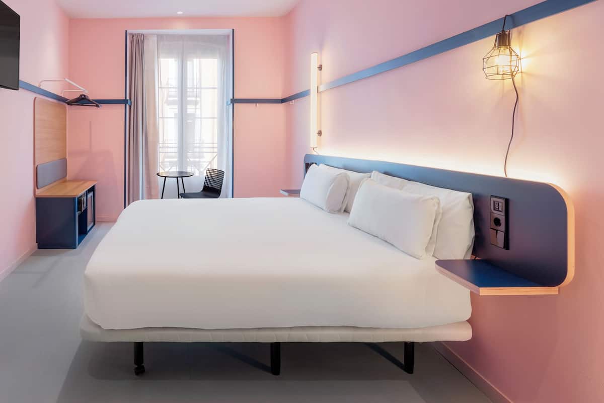 A modern hotel room with a large bed, bedside tables, a desk, and a chair.