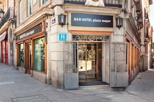 The exterior of B&B HOTEL plaza mayor with a shop entrance and a blue handicap accessibility sign.