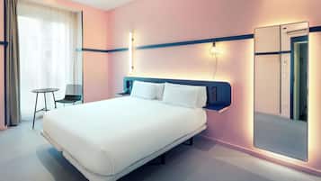 Una habitación de hotel moderna con una cama grande, una mesita de noche, una silla y un espejo amplio.