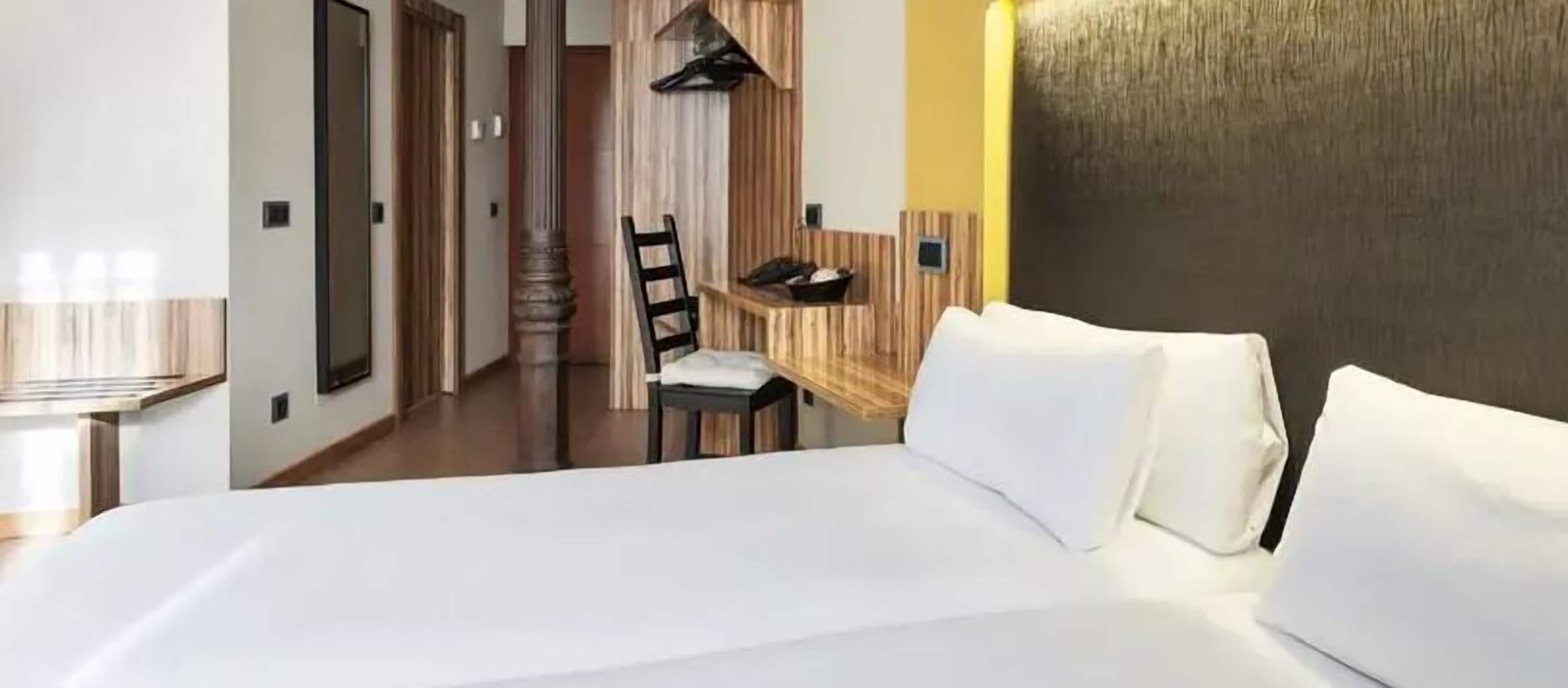 A hotel room with a large bed, a wooden headboard, a small desk with a chair, and a mirror.
