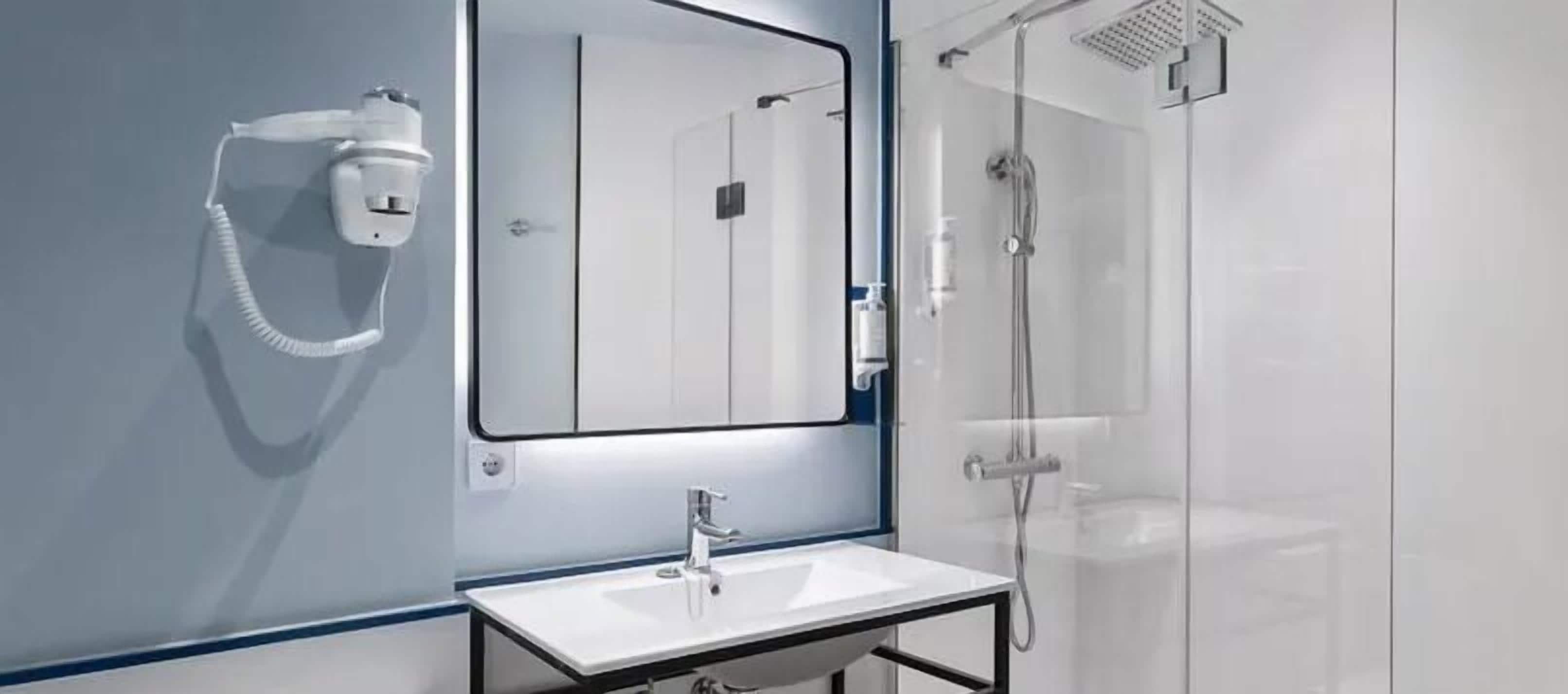 Un baño moderno con un lavabo blanco, un espejo grande y una cabina de ducha de vidrio.