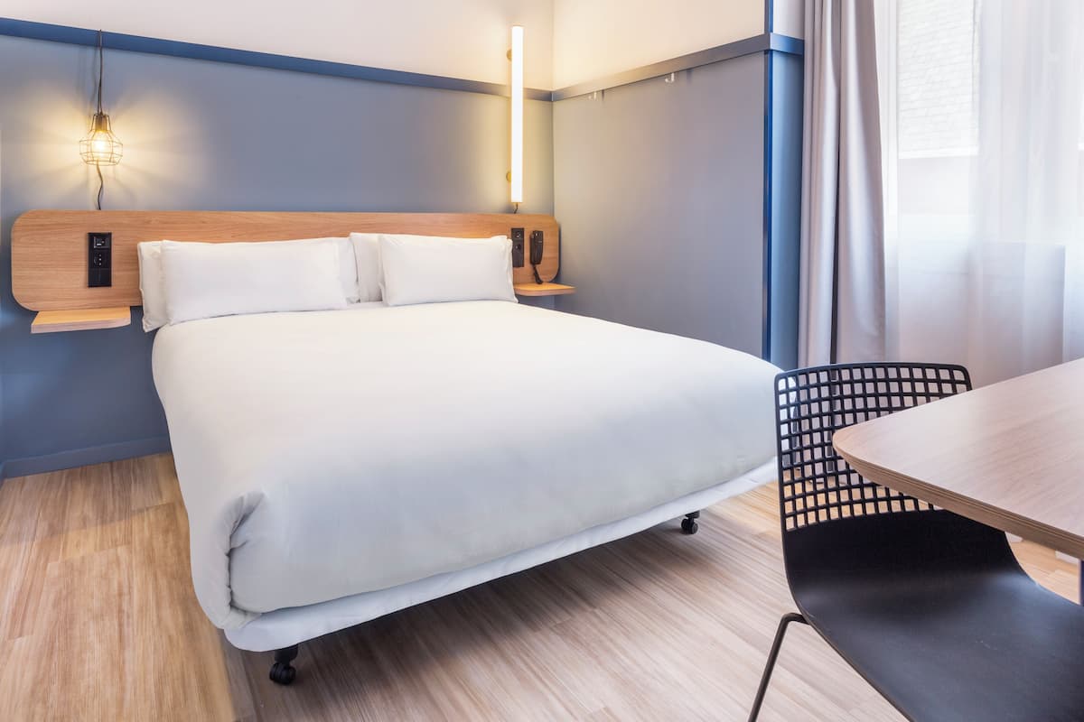 A hotel room with a bed, bedside table, lamp, and a chair.