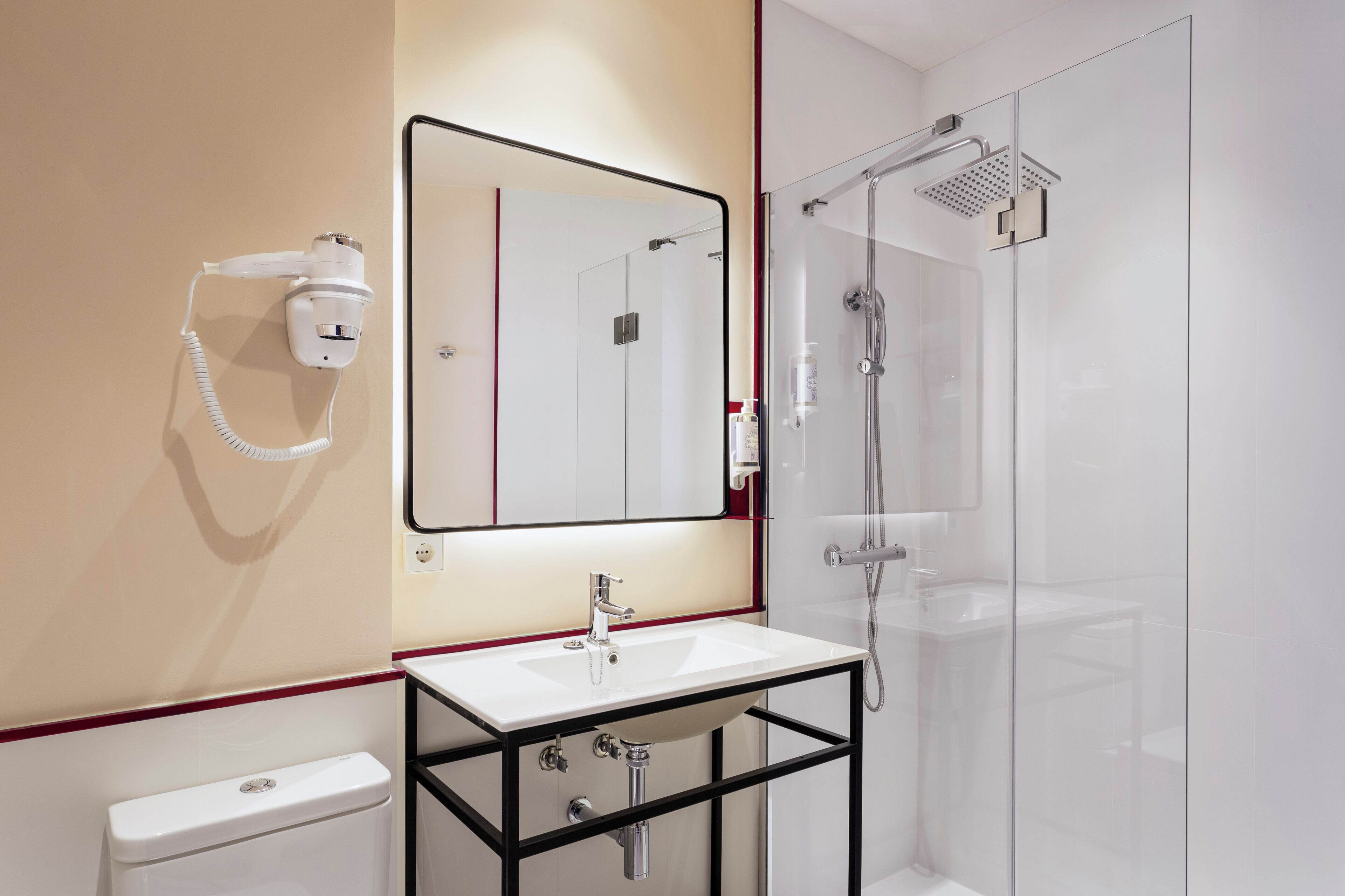 Une salle de bain moderne avec un lavabo blanc, un miroir, un sèche-cheveux, une douche en verre et des toilettes.