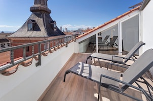 A rooftop terrace with a view of the city skyline, a wooden floor, and a glass door leading to a dining area.