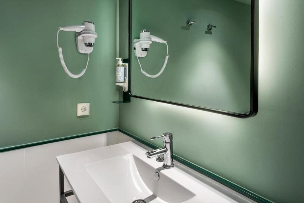 Un baño con un lavamanos blanco, un espejo y dos cabezales de ducha manuales blancos montados en la pared.