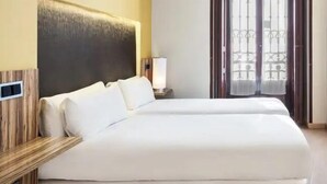 A hotel room with a large bed, a bedside table, a lamp, and a window with curtains. - B&B Hotel Madrid Centro Plaza Mayor (Madrid)