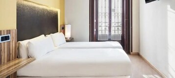 A hotel room with a large bed, a bedside table, a lamp, and a window with curtains.