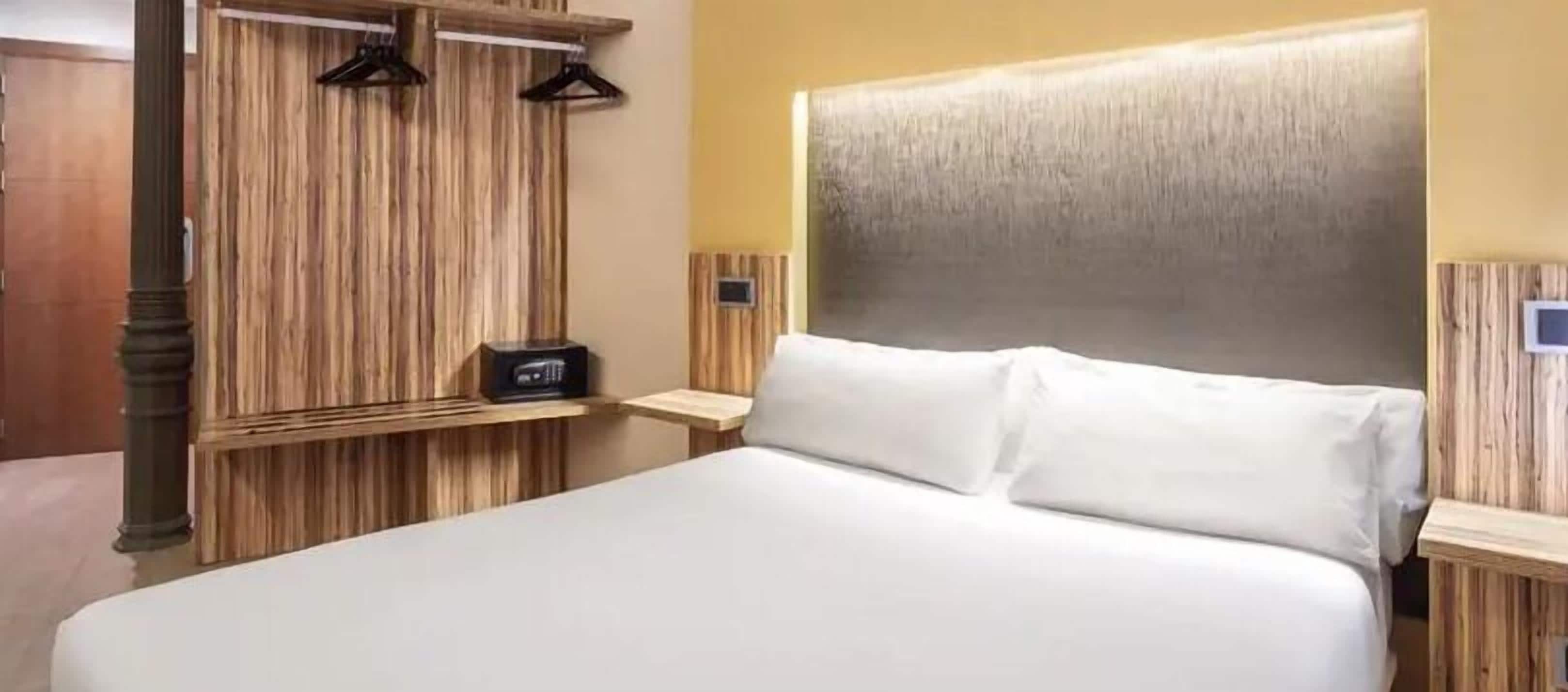 Una habitación de hotel con una cama grande, cabecero de madera y una mesita de noche con una radio.