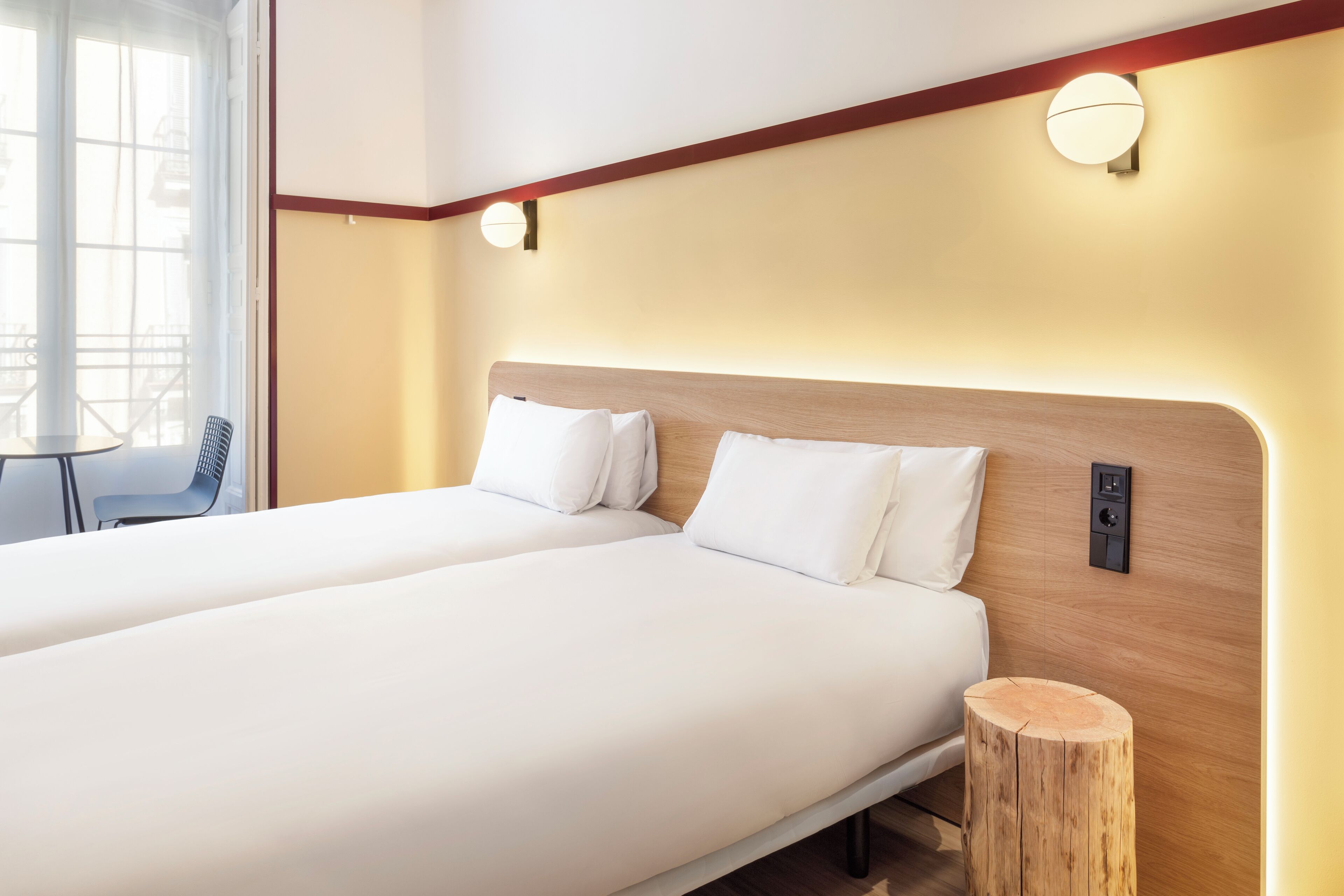 A double bed with white bedding, a wooden headboard, and two wall-mounted light fixtures.