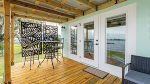 Une terrasse couverte avec un plancher en bois, des chaises en métal et une table.