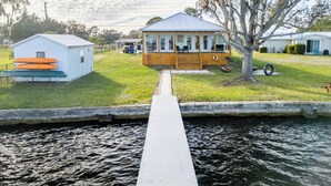 Une propriété située au bord de l’eau, avec un quai menant à une maison dotée d’une véranda, d’un petit abri de jardin et d’un arbre.