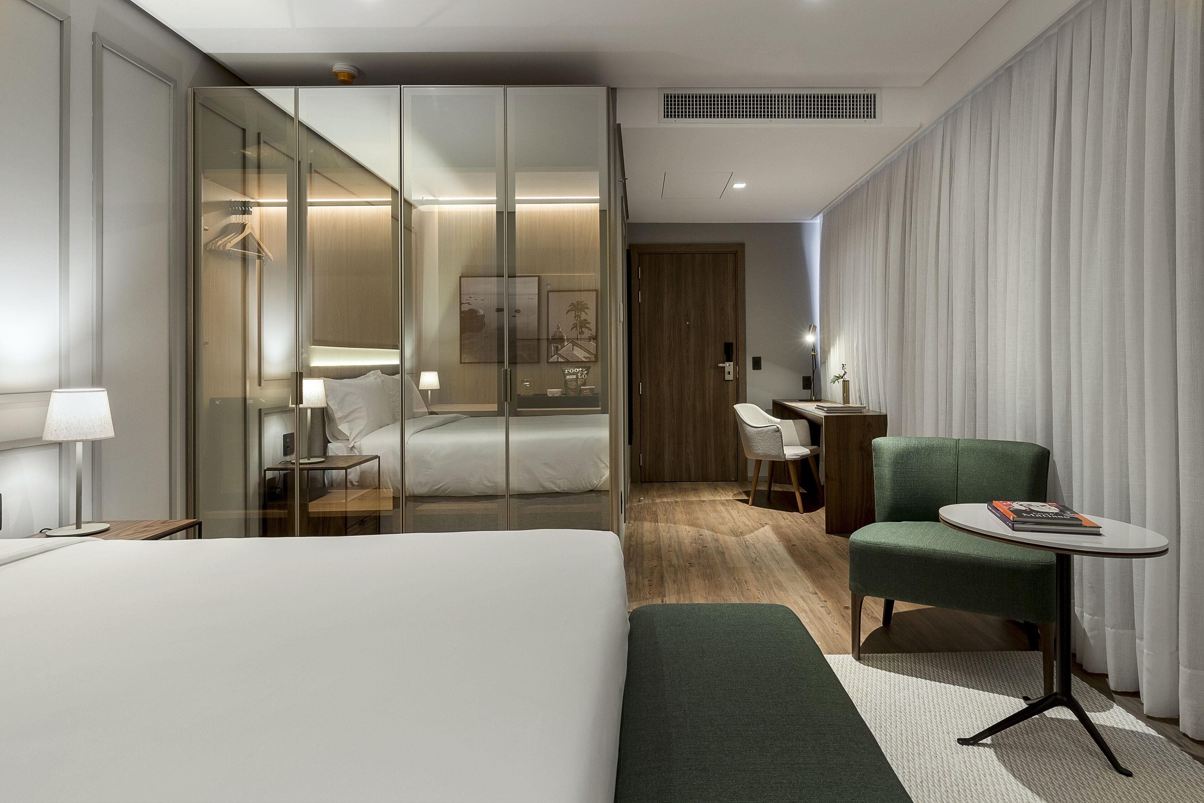 A hotel room with a large bed, a desk, a chair, and a small table with a book.