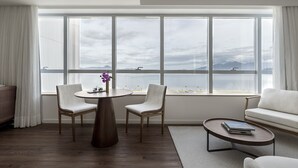 Una habitación moderna con un ventanal grande, una mesa redonda con sillas, un sofá y una pequeña mesa auxiliar.