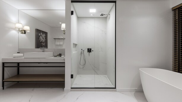 Un baño moderno con ducha envuelta en vidrio, una bañera grande y un tocador con espejo e iluminación.