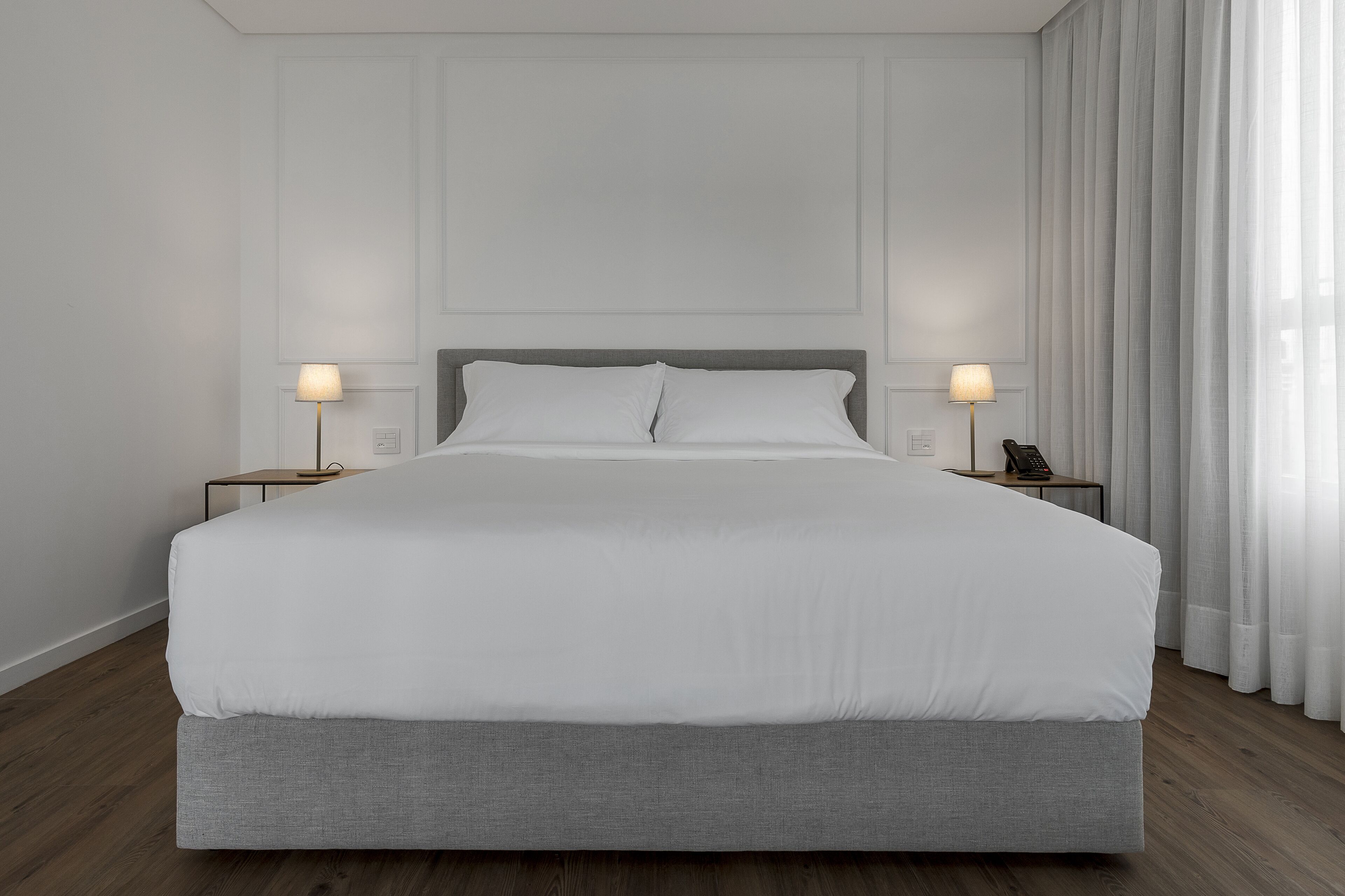 Una cama grande con ropa de cama blanca, dos mesitas de noche con lámparas y un suelo de madera.