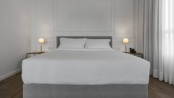 Una cama grande con ropa de cama blanca, dos mesitas de noche con lámparas y un suelo de madera.