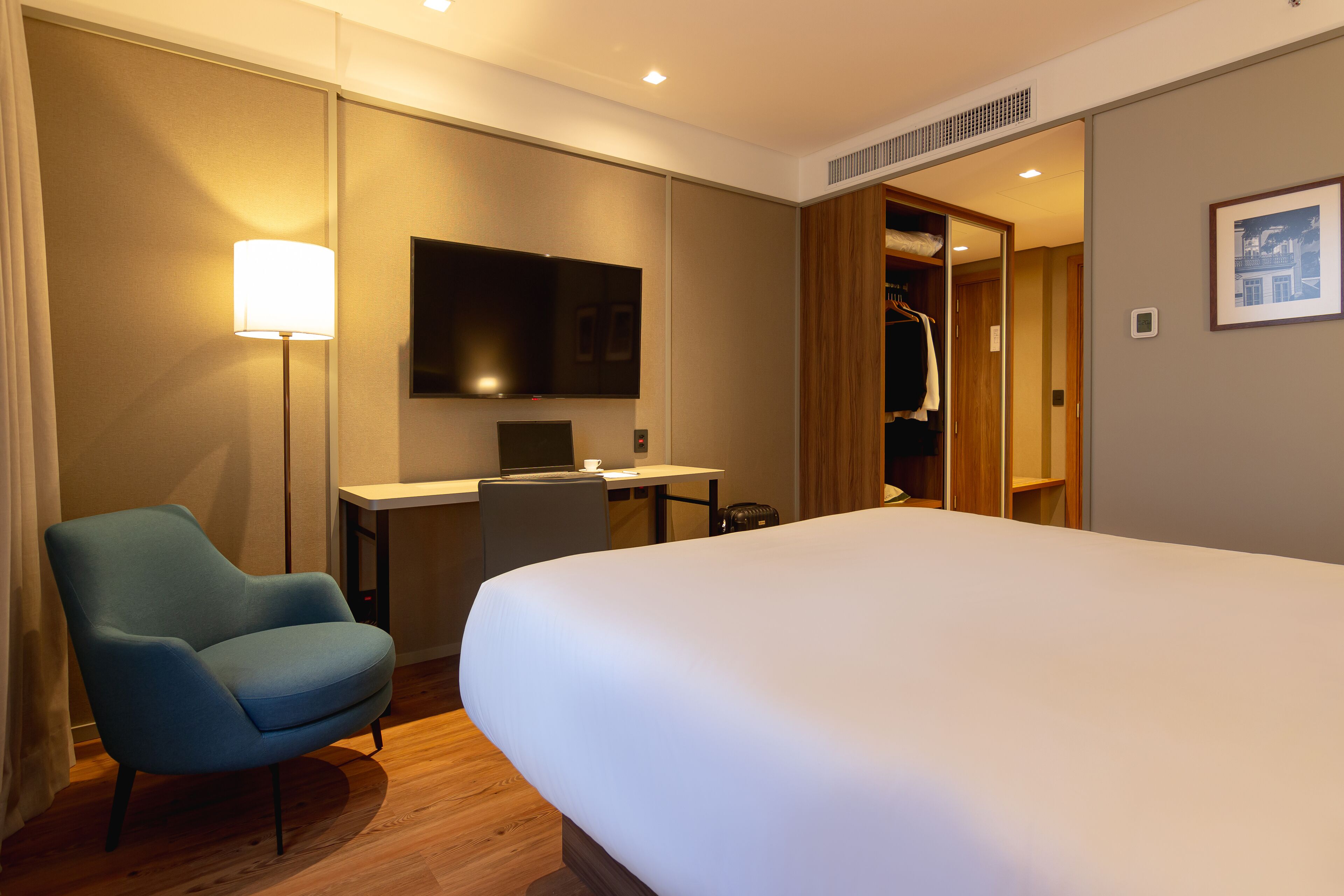 Une chambre d’hôtel avec un grand lit, un bureau avec une chaise, une télévision et une armoire.