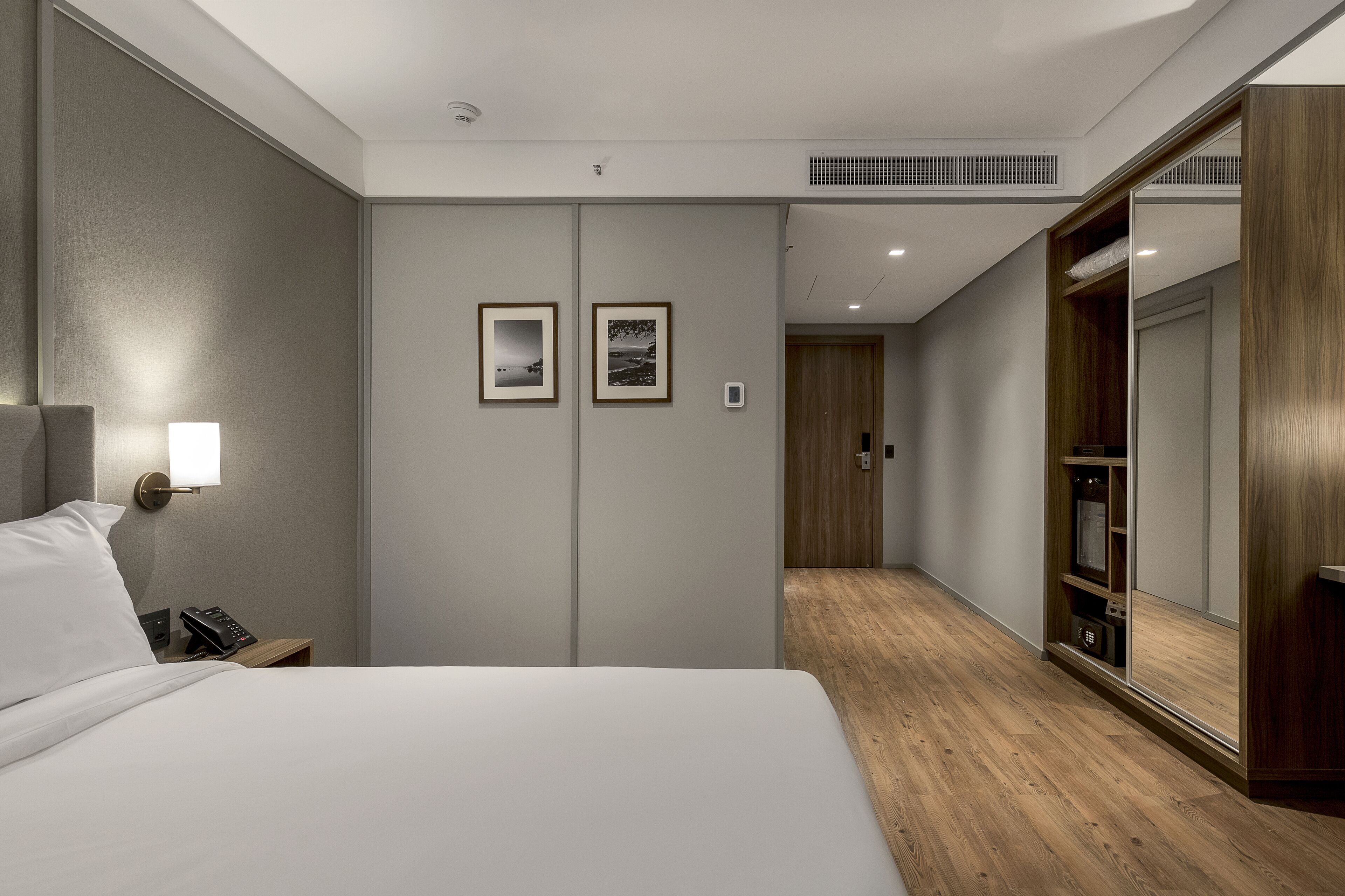A modern hotel room with a large bed, bedside table with a lamp, a phone, and two framed pictures on the wall.