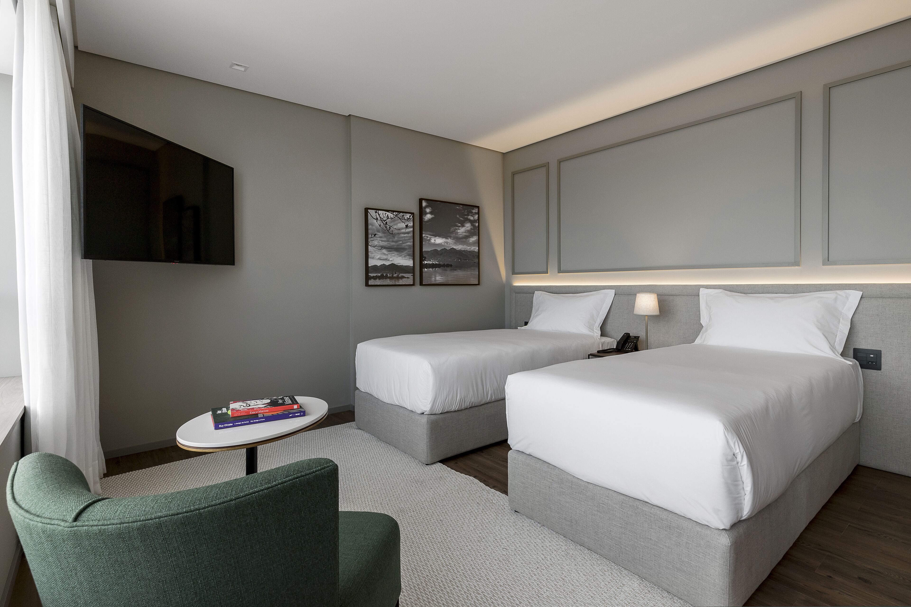 A hotel room with two beds, a small table, a chair, and a TV on the wall.