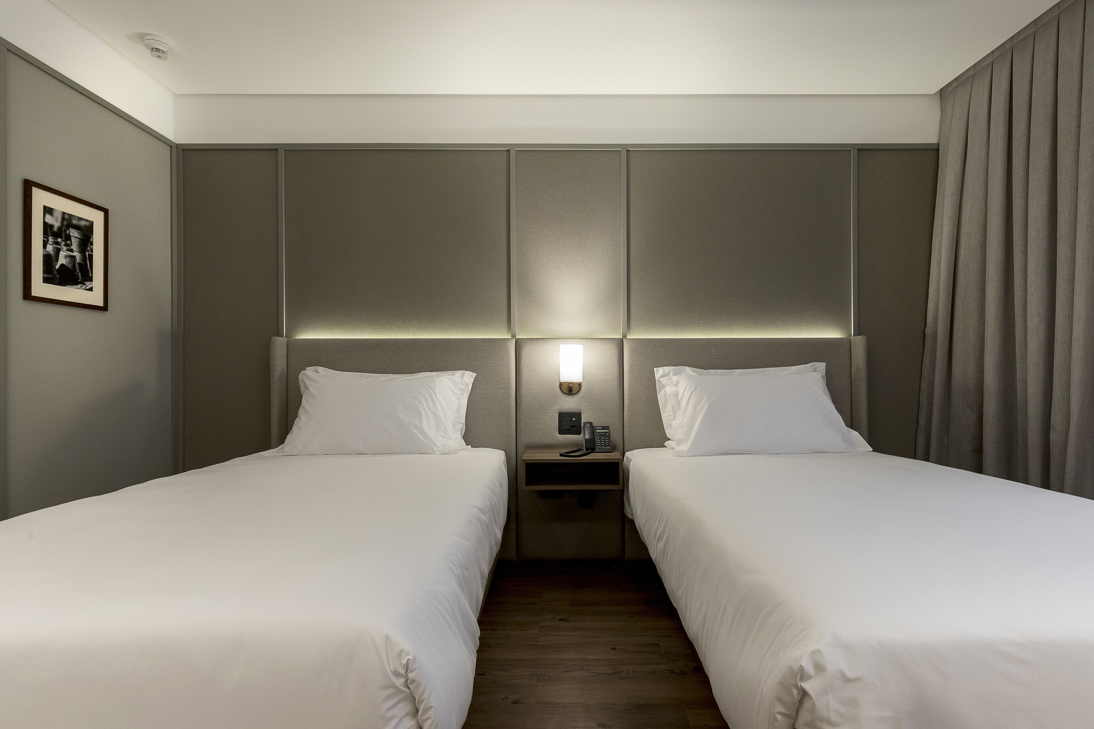 Habitación de hotel con dos camas individuales, una mesita de noche con teléfono, y una lámpara de pared.
