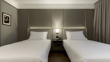 Habitación de hotel con dos camas individuales, una mesita de noche con teléfono, y una lámpara de pared.