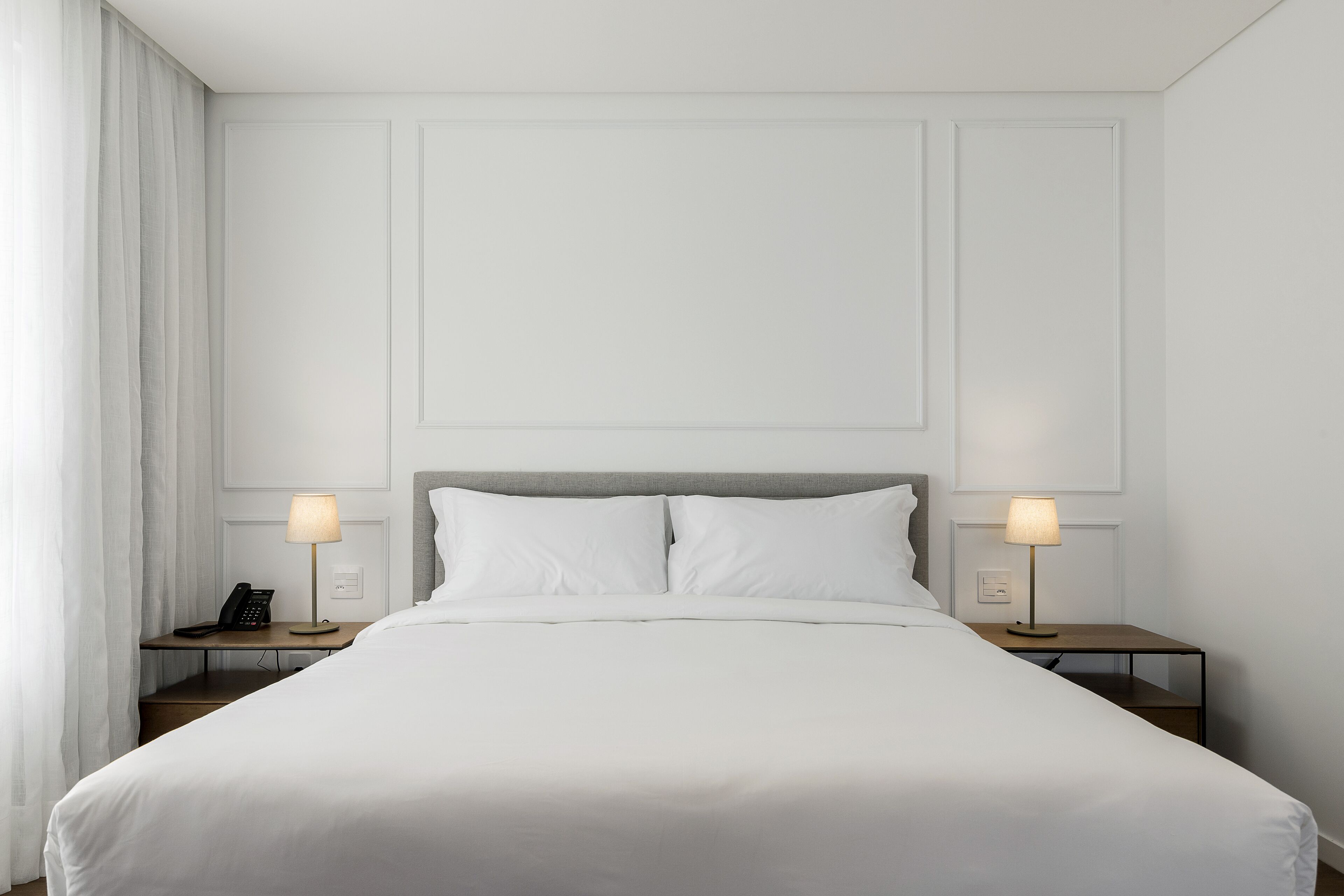A neatly made bed with white linens, two bedside tables with lamps, and a telephone on the left table.