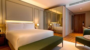 Una habitación de hotel con una cama grande, un banco verde, una mesita y un espejo.