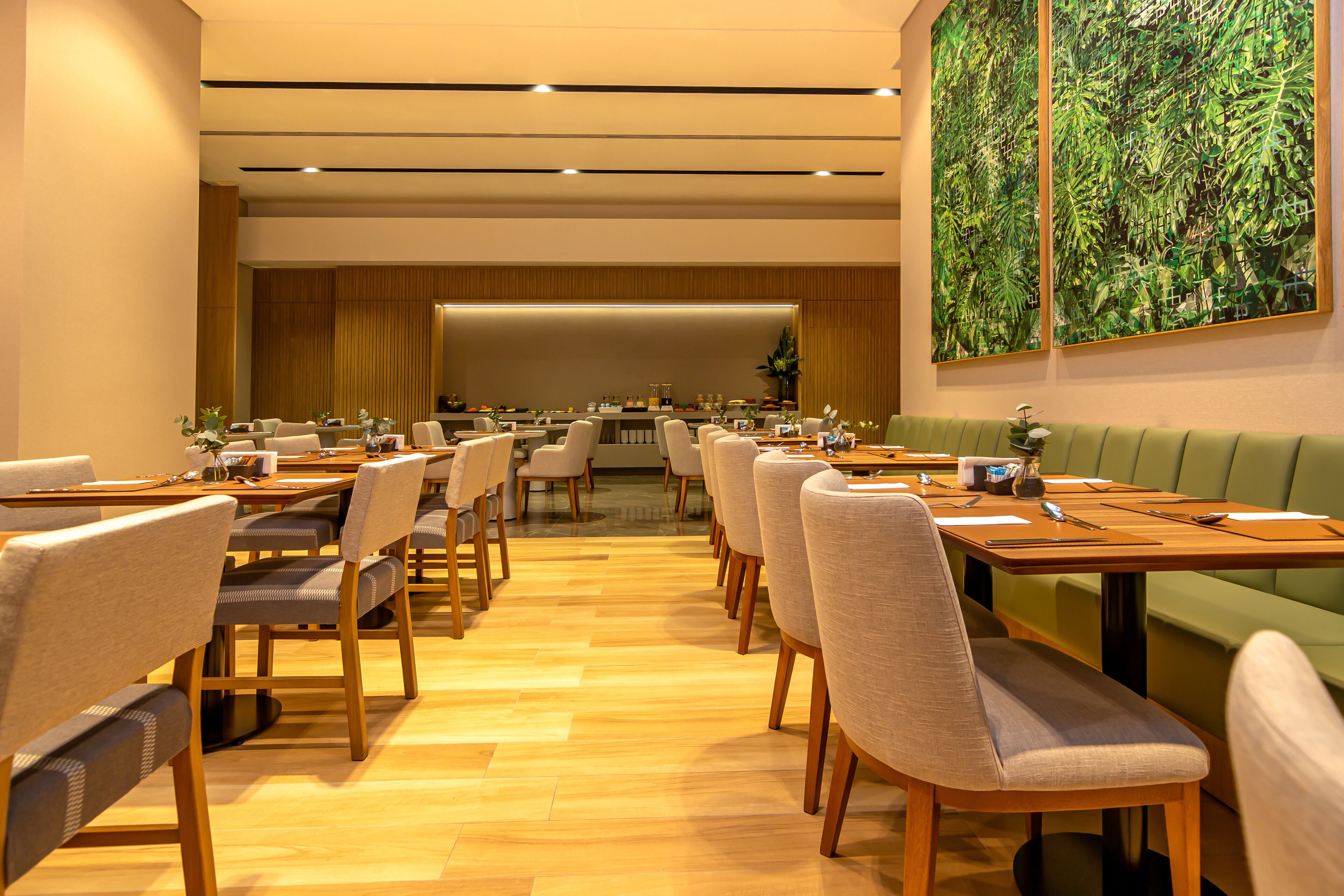 Un espace repas moderne avec des tables et des chaises en bois, un coin salon avec des banquettes vertes et un grand tableau abstrait accroché au mur.