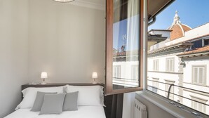 Ein Hotelzimmer mit einem Bett, zwei Nachttischlampen, einem Fenster mit Blick auf Gebäude und einer Heizung.