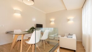 Ein modernes Wohnzimmer mit einem Glastisch, weißen Stühlen, einem weißen Sofa und einem Fernseher.