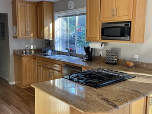 A kitchen with wooden cabinets, a stainless steel microwave, a gas stove, and a window with a view of greenery. - Spacious Forest Home, 3 Bedrooms, Mountain Views, 5 Min. to Jacksonville, Pets! (Jacksonville)