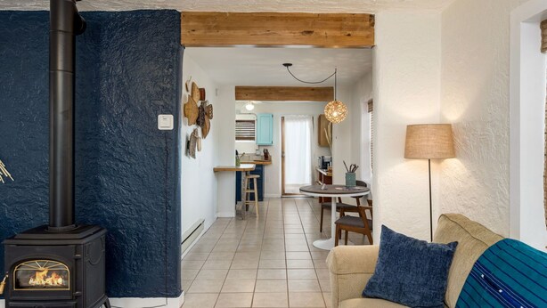 A cozy living room with a fireplace, a dining area, and a kitchen visible through an open doorway. - The Blue House (Truth or Consequences)