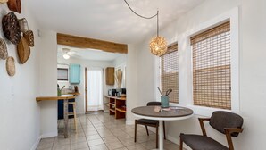 A dining area with a round table, two chairs, a hanging light fixture, and a window with bamboo blinds. - The Blue House (Truth or Consequences)