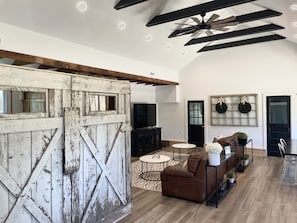 Un salon spacieux avec une grande porte en bois, un ventilateur de plafond, une cheminée et une porte noire ornée de guirlandes.