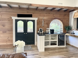 Une pièce chaleureuse avec une porte noire, des murs en bois, un comptoir blanc et un petit réfrigérateur.