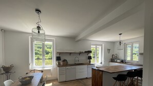 A modern kitchen with white cabinets, a wooden island, and large windows overlooking a lake. - Country house for 15 people, waterfront in the Ardennes nature park (Revin)