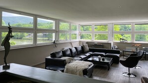 A modern living room with a large sectional sofa, a coffee table, and a view of a river and greenery through large windows. - Country house for 15 people, waterfront in the Ardennes nature park (Revin)