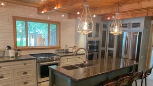 Une cuisine moderne dotée d’un îlot central, d’appareils électroménagers en acier inoxydable et de luminaires suspendus.