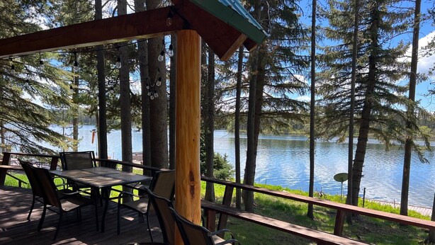 Une terrasse en bois avec une table et des chaises, donnant sur un lac bordé d’arbres.