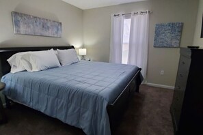 Une chambre à coucher comprenant un lit, une table de chevet, une lampe, une commode et deux œuvres d’art murales.