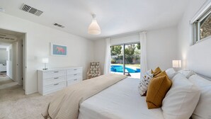 Ein Schlafzimmer mit einem großen Bett, einem Schminktisch, einem Fenster mit Blick auf einen Swimmingpool und einem Deckenventilator.