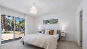 Ein Schlafzimmer mit einem großen Bett, zwei Nachttischen, einem Fenster und Blick ins Freie.