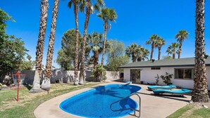 Ein Garten mit Swimmingpool, Palmen und Gartenmöbeln.