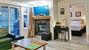 Ein Wohnzimmer mit Kamin, einem darüber montierten Fernseher und Blick durch eine Glastür nach draußen.
