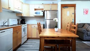 Eine kleine Küche mit Holzausbau, einem Edelstahlkühlschrank, einer Mikrowelle und einem Esstisch mit Stühlen.