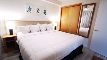 A neatly made bed with white bedding, a wooden headboard, and a nightstand with a lamp. There are three framed botanical prints on the wall above the bed.