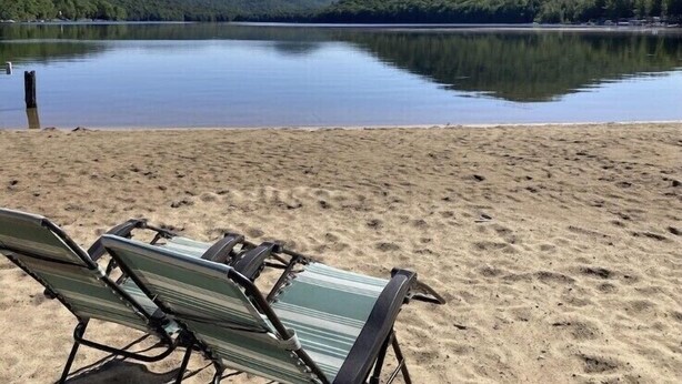 Una playa con dos sillas de descanso y un lago tranquilo con una colina boscosa al fondo.