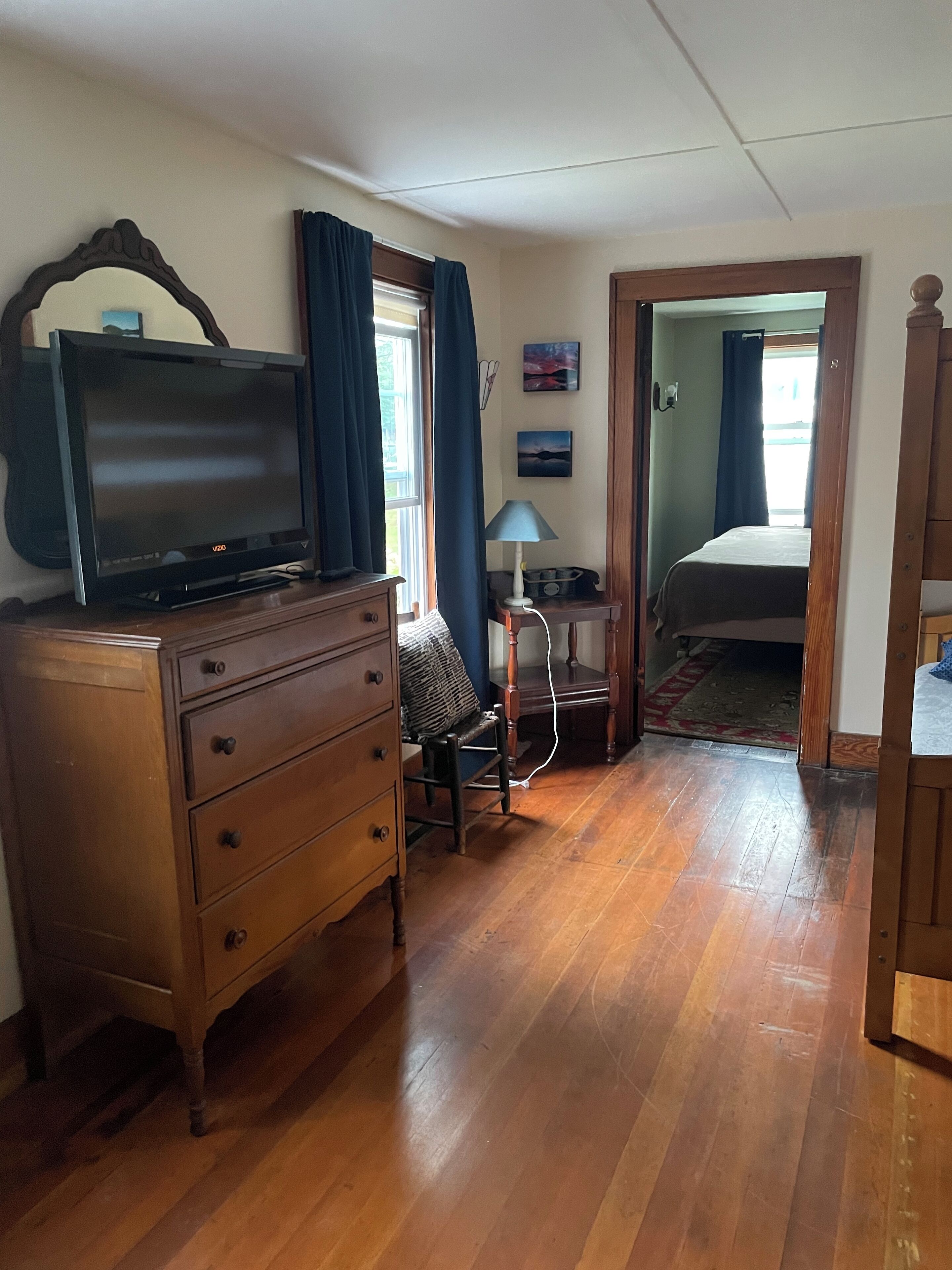 Une pièce comprenant une commode en bois, un téléviseur, une lampe et un lit.